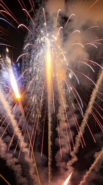 Vertical video: Firing fireworks lighting sky at park for show, showing golden burst portrait phone