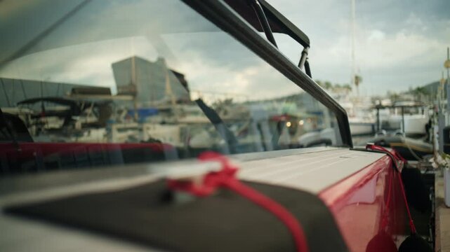 Low angle close up of the red side of a yacht docked at Port Vauban in Antibes, with calm marina water, blurred boats, and cloudy Mediterranean sky in the background