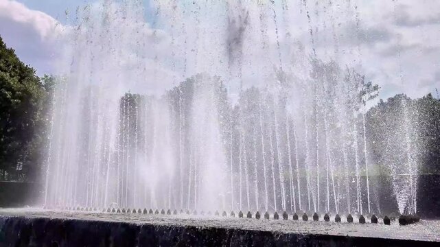 Powerful water jets from a large city park fountain spraying high into the air on a beautiful sunny summer day, creating a refreshing and dynamic urban landscape