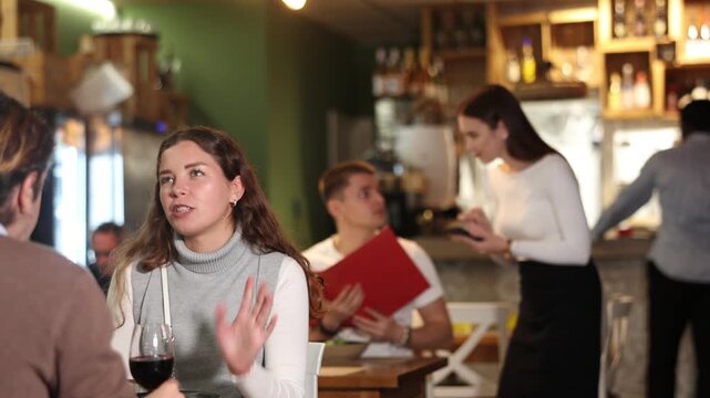 Girl in cafe sits opposite male companion, has nice conversation and discusses news of day. Cozy atmosphere of cafe, meeting place for friends, business partners, colleagues.