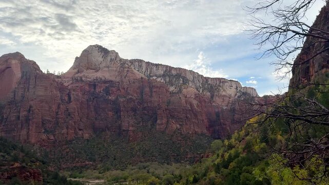 Massive sandstone cliffs rising above Zion National Park in Utah, Wide scenic travel video shows layered red canyon walls beneath textured clouds
