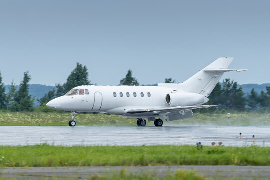 White business jet moves along a wet runway after rain