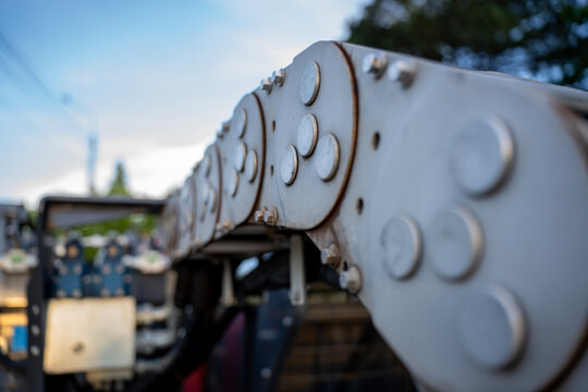 Close up of a heavy duty steel flexible cable carrier track on industrial machinery, protecting cables and hydraulic hoses with selective focus.