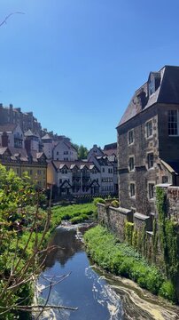Scenic view of Dean Village along the Water of Leith in Edinburgh, historic stone houses reflected in the river, peaceful riverside landscape, charming Scottish heritage, picturesque neighborhood