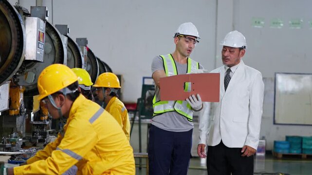 Industrial team collaborating in factory setting engineers discussing project plans with safety gear on