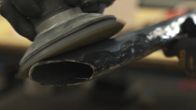 A worker creates texture on a metal pipe with a grinder, grinding off excess metal so that the pipe can later be painted to look like wood