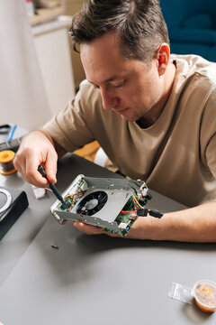 Vertical portrait of technician male working on electronic device, holding computer hardware with exposed cooling fan, performing repairs and maintenance on tech equipment in modern workshop.