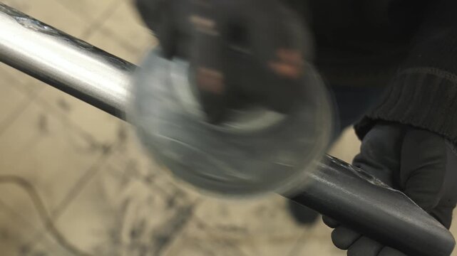 A worker creates texture on a metal pipe with a grinder, grinding off excess metal so that the pipe can later be painted to look like wood