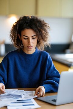 Young woman managing household bills at kitchen table with laptop for personal finance background and budgeting design