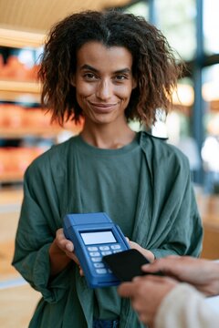 Smiling cashier holding a card reader while customer taps a smartphone for contactless payment at retail checkout for store background