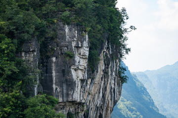 A view of the steep rocky cliffs covered in lush green vegetation located near the Three Gorges Reservoir in Yichang China during a bright summer day © AS_SleepingPanda