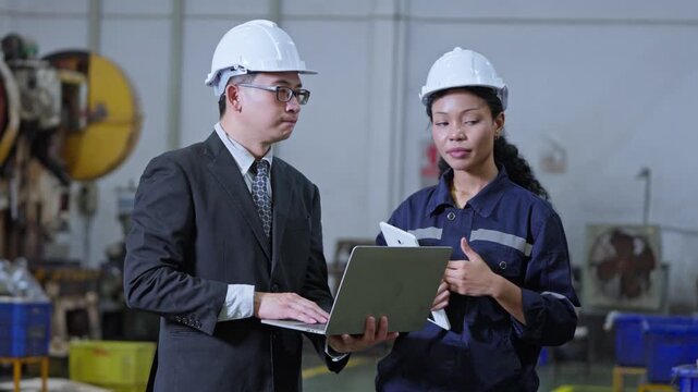 Professional engineers discussing project details in industrial setting with laptops and safety gear