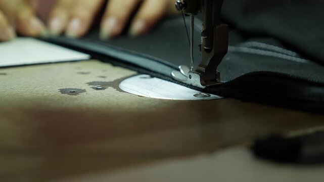 A seamstress guides fabric under a sewing machine needle beside sewing machine parts. Tailoring.