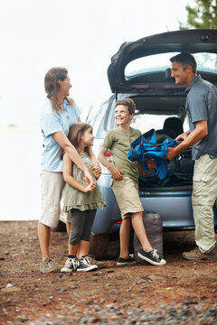 Happy, family and camping with car in nature for travel, roadtrip or outdoor holiday together. Children, mom and dad unpacking vehicle with gear for adventure, sightseeing or bonding in wilderness