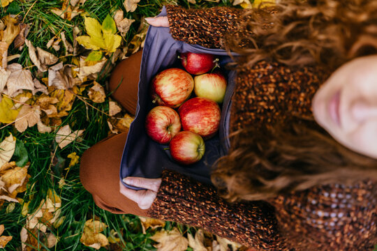 Vertical overhead view of red-haired woman carrying fresh apples in reusable fabric apron