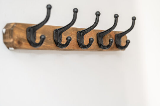 Rustic wooden wall coat rack with five black metal hooks.Close-up of a handmade rustic coat hanger mounted on a white wall.Ideal concept for home interior design, hallway organization, and rustic furn
