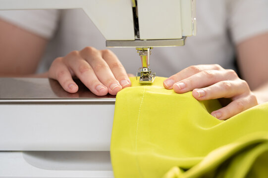 Woman hands carefully guiding a vibrant lime green fabric through a sewing machine on a clean workspace.Independent fashion designer or small business owner creating a handmade garment using a profess