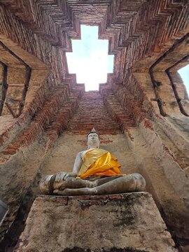 Buddha Statue in Ancient Temple: A serene Buddha statue sits in contemplation within the weathered brick structure of an ancient temple.