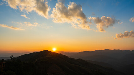 Golden sunrise over mountain hills with dramatic clouds and warm morning light.