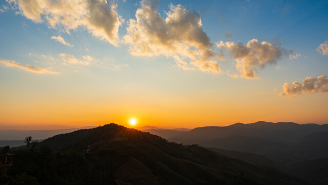 Golden sunrise over mountain hills with dramatic clouds and warm morning light.