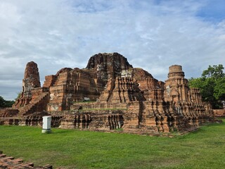 Fototapeta premium Ancient Ayutthaya Ruins: Majestic brick ruins of an ancient temple stand weathered against a cloudy sky, remnants of a bygone era hinting at stories of history and devotion.