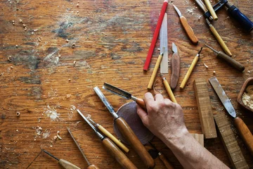 Wood carving tools in craftsman hands on workbench. Woodcarving, joinery, timber carpentry and woodwork background top view. © juliasudnitskaya