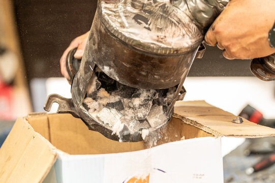Mechanic emptying a damaged car catalytic converter or DPF filter core into a box. Automotive waste management, exhaust system recycling, and precious metal recovery concept.