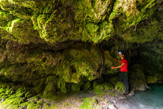 Adventurer exploring a mossy, rocky grotto with a headlamp, experiencing an outdoor adventure lifestyle near the Sorna river, Rovereto, Vallagarina, Brentonico plateau, Trentino, Italy.