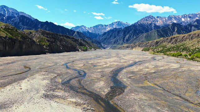 Wide aerial view of a braided river valley cutting through a vast mountain canyon under a clear blue sky in Xinjiang, China.