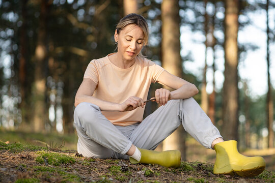 Calm woman sitting on forest ground enjoying quiet moment, smiling female finding emotional balance in nature, practicing mental grounding in woodlands. Solitude, inner peace and outdoor activity, 