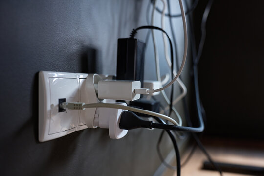 Wall outlet with multiple power adapters, plugs and connected cables for electronic devices
