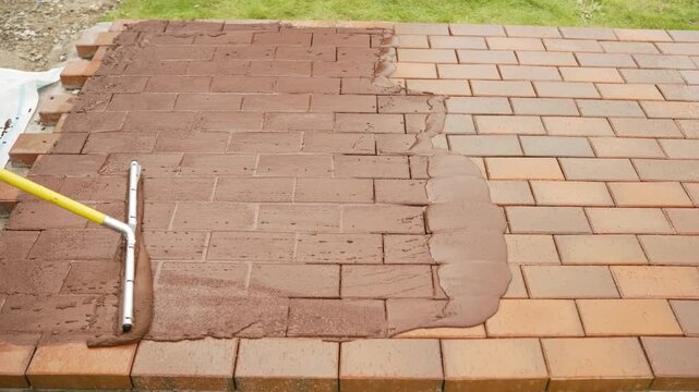 Paving Stone Jointing Process. Video shows worker applying and spreading sand mortar between paving stones using a squeegee tool to fill gaps and stabilize the patio surface