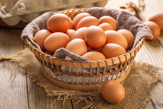 Basket full of fresh brown eggs on a rustic wooden table with a whisk and shell fragments
