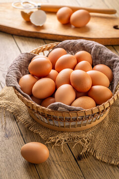 Basket full of fresh brown eggs on a rustic wooden table with a whisk and shell fragments