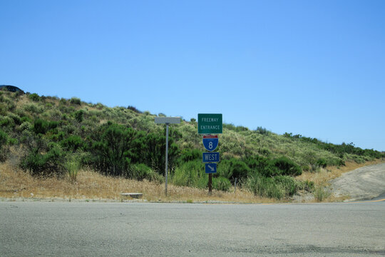 Freeway entrance sign pointing to Interstate-8 West along a rural road against a grassy hillside in California; copy space