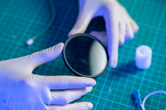 A person wears gloves while holding a round mirror in a lab