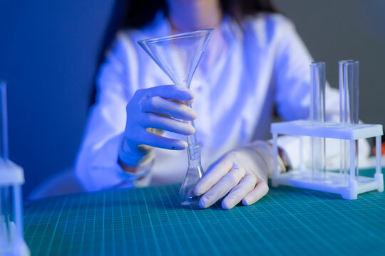 A person in a lab coat and gloves handles glassware while working on vaccine research in a laboratory