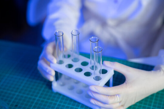 A person in a lab holds a test tube rack with several empty test tubes for conducting vaccine research