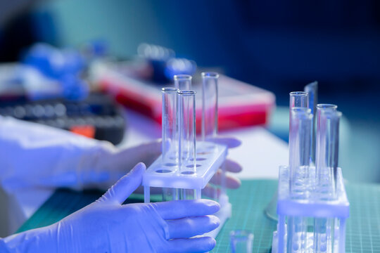 Technician in gloves handles test tubes holding vaccine samples in a laboratory with equipment nearby