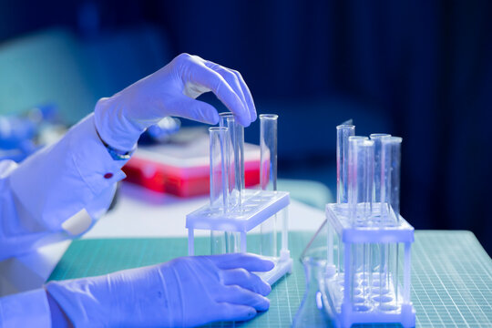A researcher in gloves handles test tubes with vaccine samples on a laboratory table in a medical facility