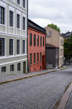 Through Gr&uuml;nerl&oslash;kka, a cobblestone lane curves past quiet buildings as overcast light softens facades, extending street perspective through the architecture of Oslo, Norway.