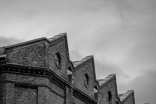 Against a cloudy sky, a roofline in Gr&uuml;nerl&oslash;kka reveals brick rooftops and sawtooth architecture, forming an industrial silhouette in monochrome Oslo, Norway.