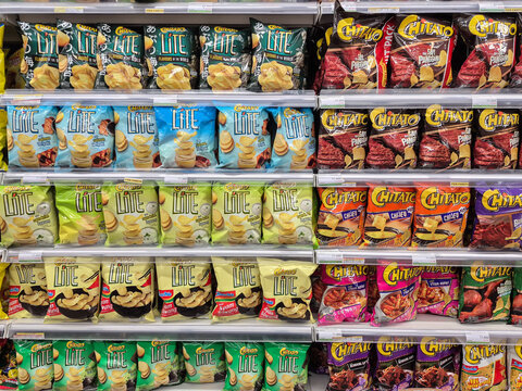 Various brands and logos of potato chip bags on supermarket shelves, displaying snack products in a grocery store aisle.
