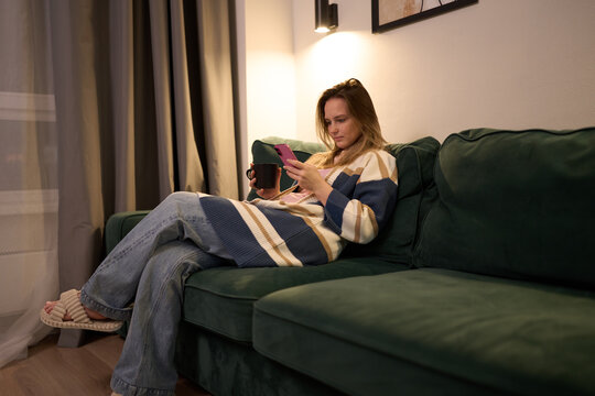 Woman relaxing with smartphone and coffee on green sofa at home