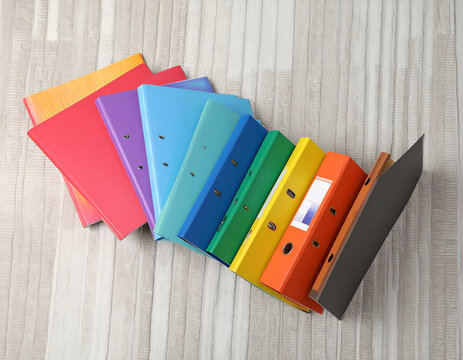 Colorful ring binders arranged in a fan shape on a textured rug. Office stationery, colorful archive folders, and organization supplies for school or business.