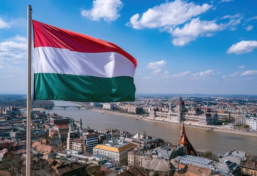View of the Hungarian flag flying over the city of Budapest by the Danube River during a sunny day with clouds in the sky