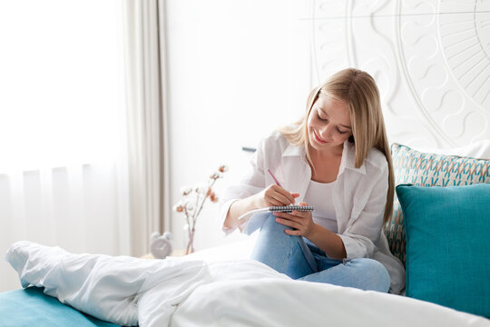 Young woman relaxing in bed. Girl writing in journal, drawing. Art therapy, self-care, female wellness, morning routine in cozy home. Slow living, mindfulness, analog lifestyle, digital detox