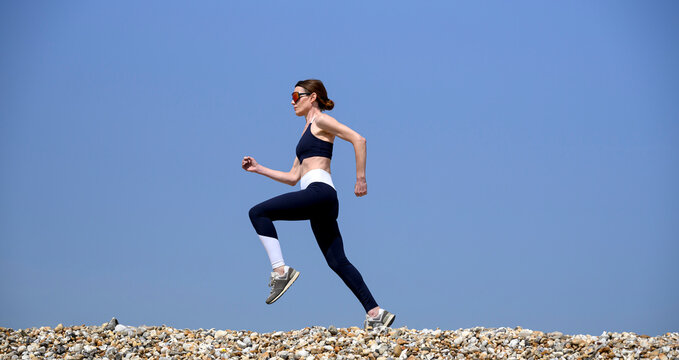 sporty woman running on a pebble beach