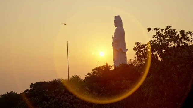 Artistic shot of the Lady Buddha statue at sunset, enveloped by a vibrant orange halo, creating a spiritual and dramatic silhouette in Da Nang, Vietnam.