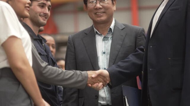 Close-up shot of business partners and industrial engineers shaking hands inside a modern factory. Concept of successful business agreement, international partnership, corporate merger, and B2B manufa
